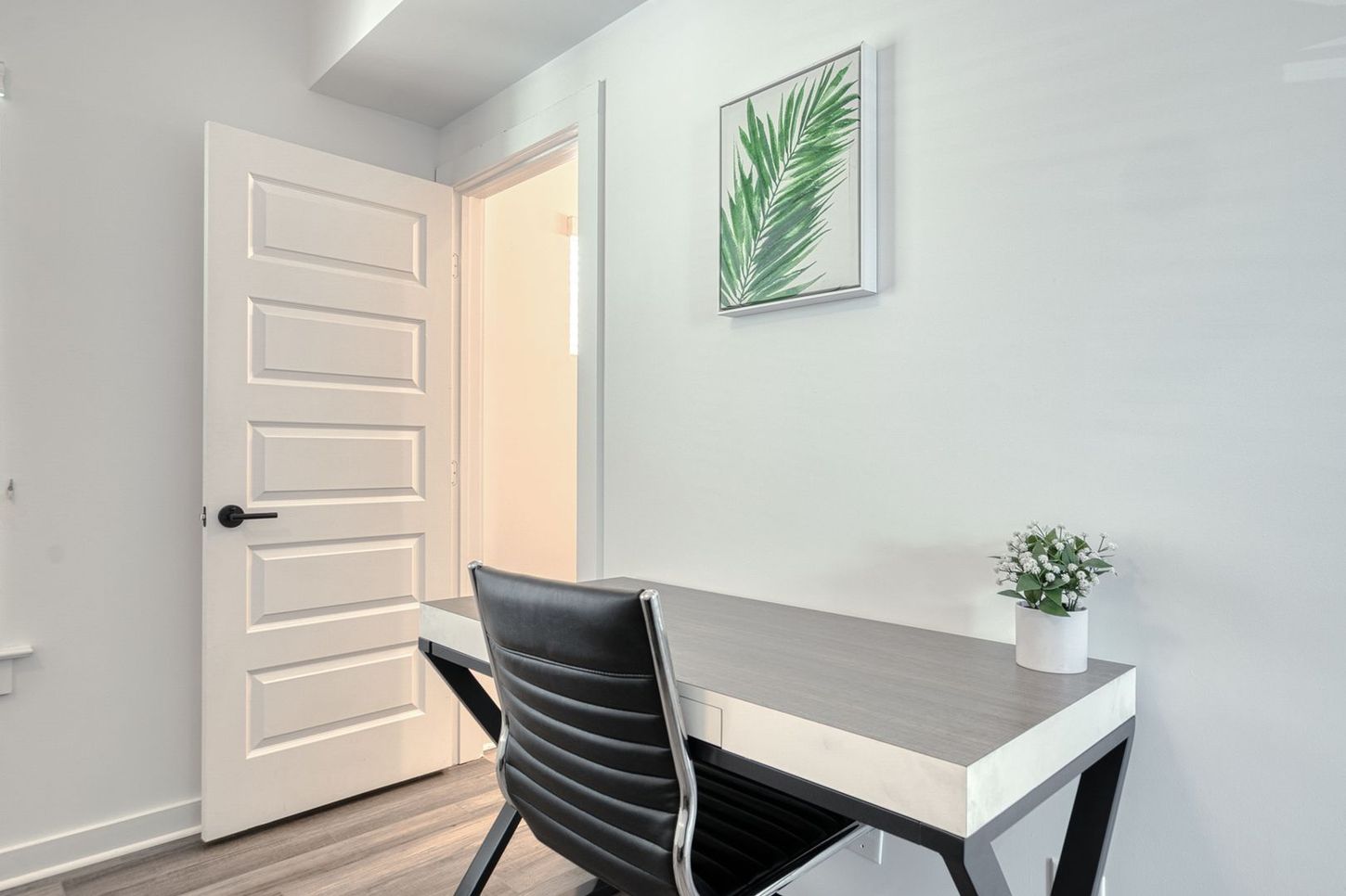 White home office with a desk, chair, artwork, and partially open door.