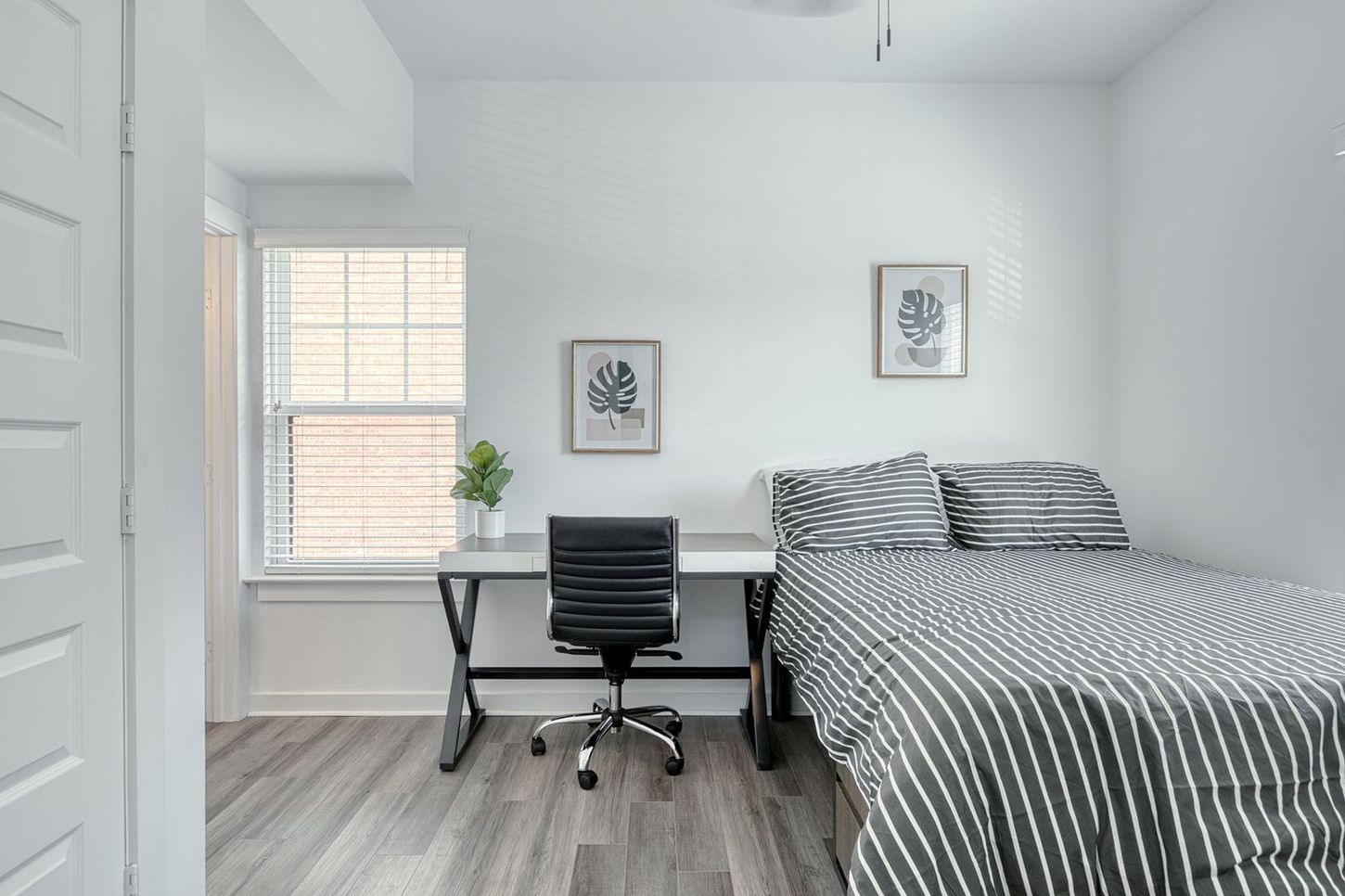 A small, modern bedroom with a desk, bed, and window.  White walls, gray floors and furniture.
