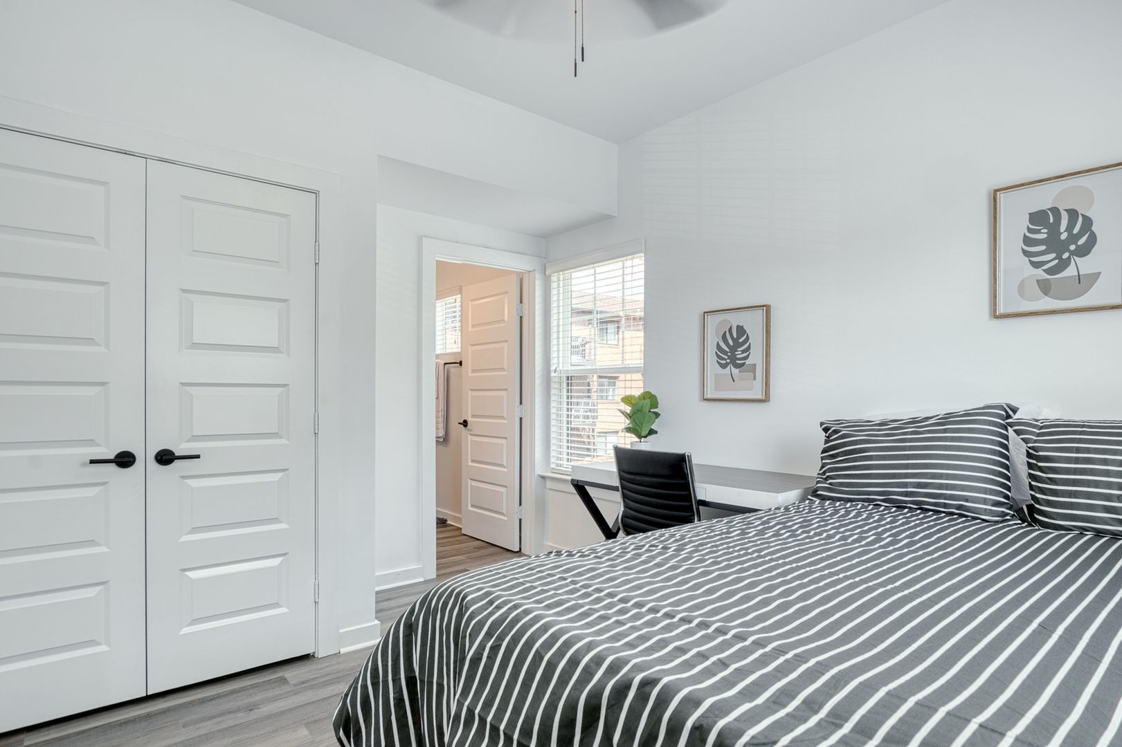 Bedroom with white walls, closet, bed with striped bedding, desk, and doorway to a bathroom.