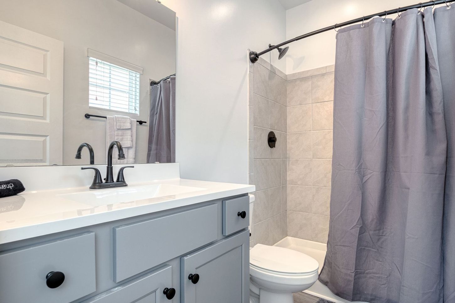 Bathroom with gray vanity, white countertop, and shower with gray curtain.