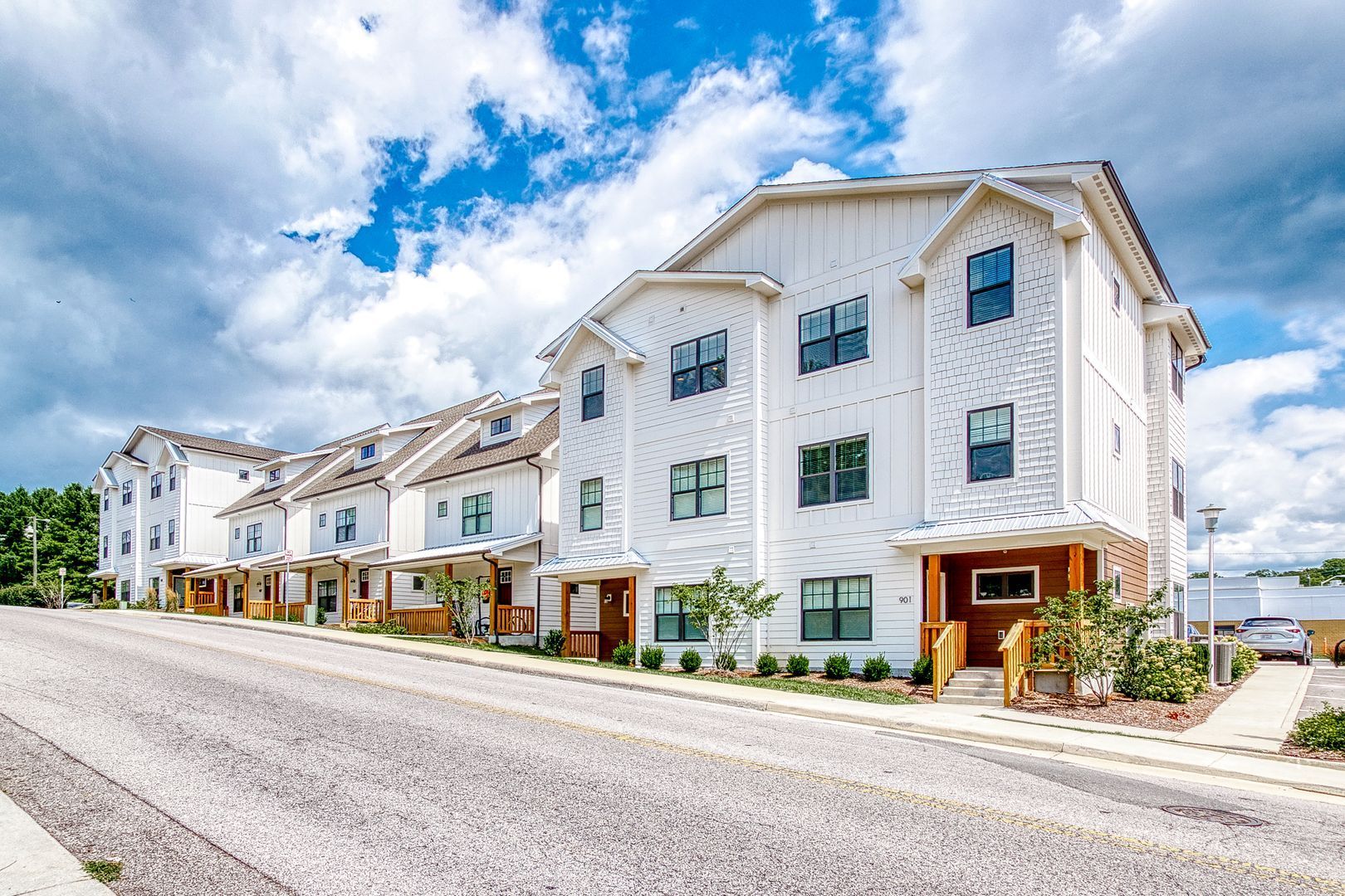 White townhouses on a slightly sloped street with blue sky and clouds in the background.