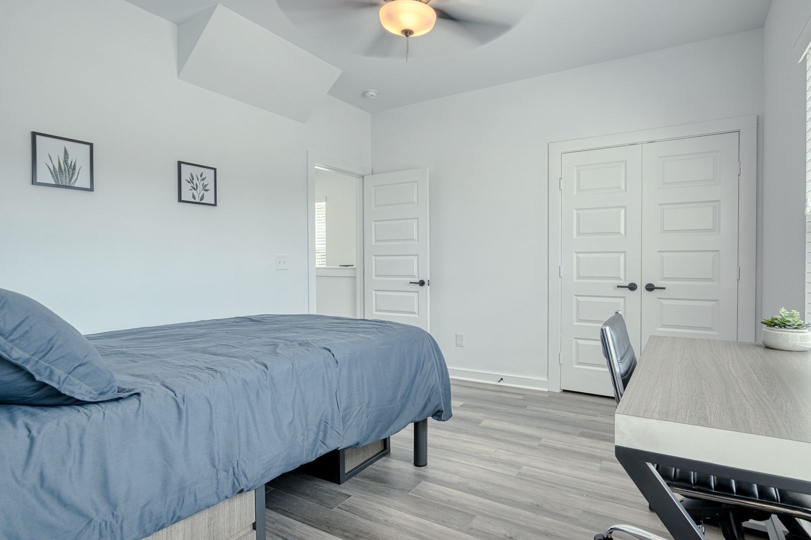 Bedroom with a blue bed, white walls, two art prints, and a desk.