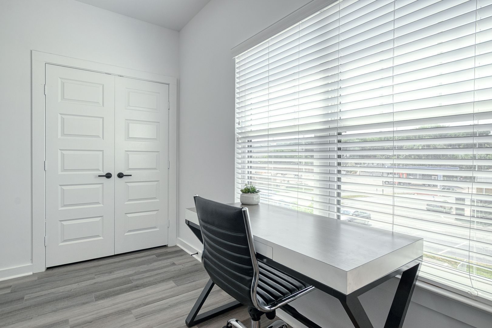 Desk and chair in a room with white walls, door, and a window with blinds.