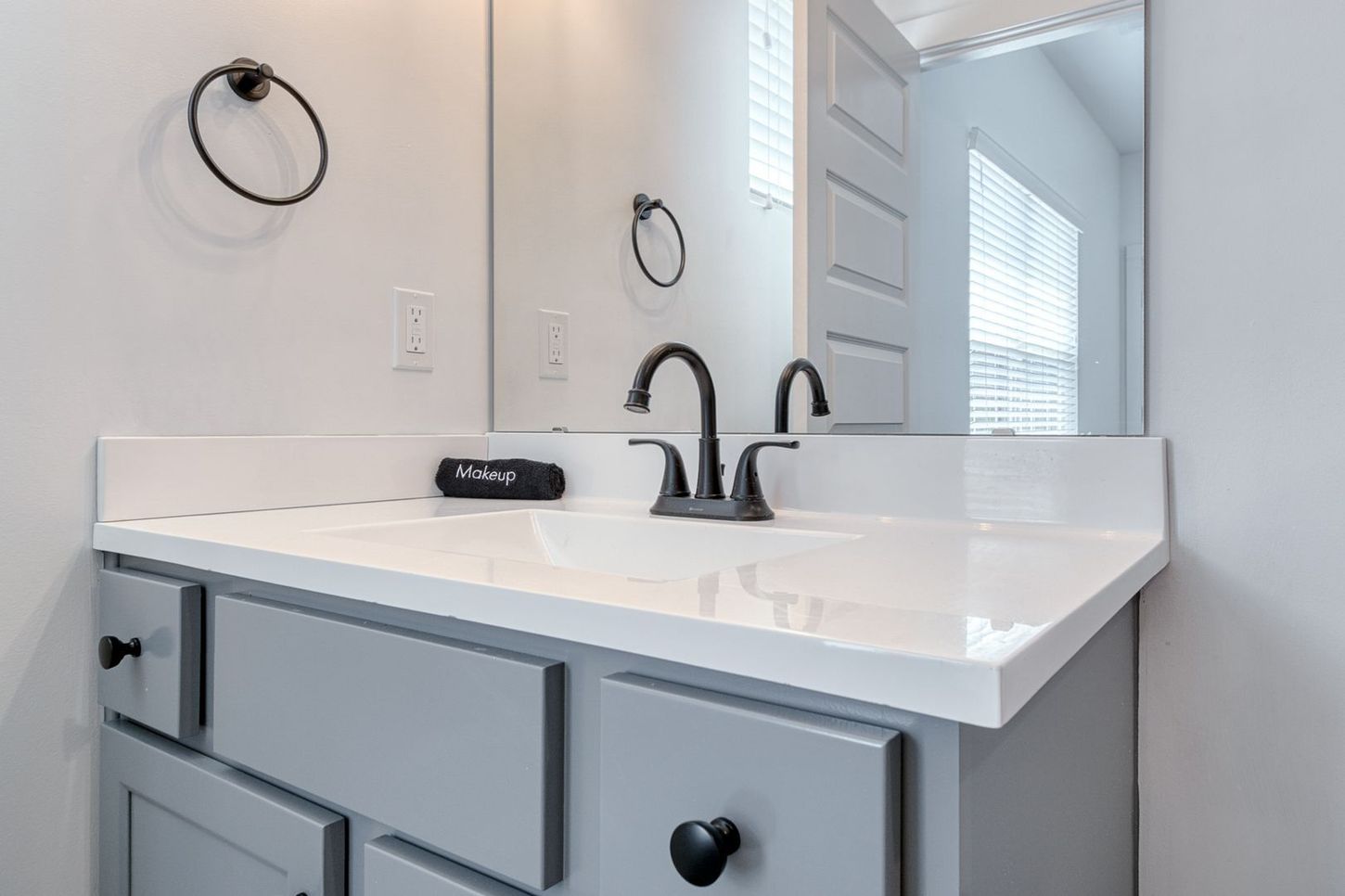 Gray bathroom vanity with white countertop, black fixtures, and mirror.