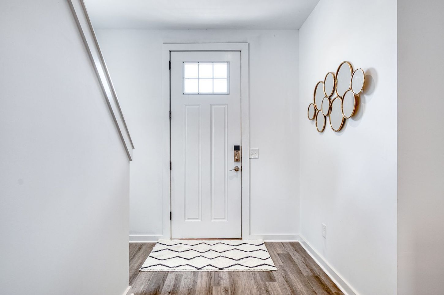 White entryway with door, patterned rug, and decorative mirrors on wall.