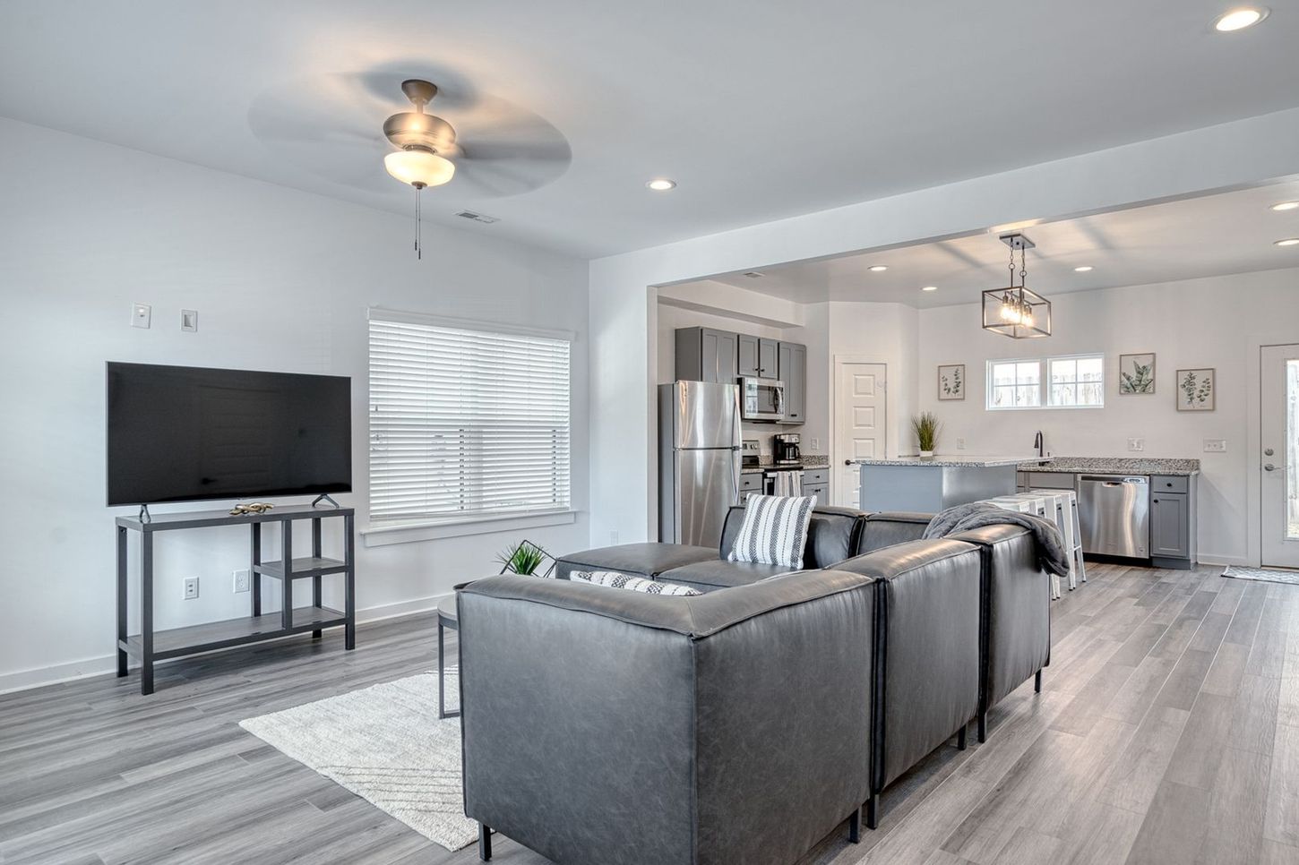 Modern living room with gray sectional sofa, TV, and open kitchen.