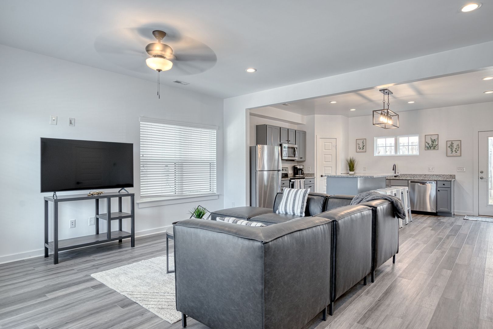Modern living room with gray sectional sofa, TV, and open kitchen.