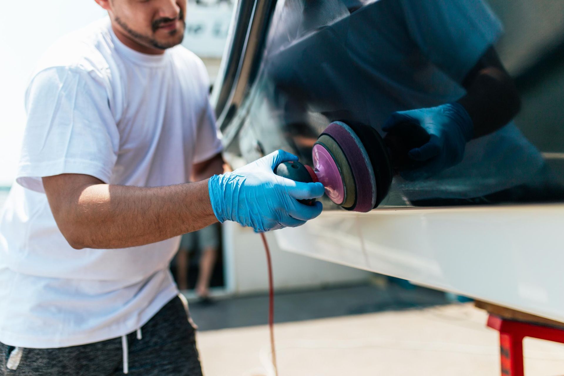 Person in blue gloves using a polisher on a boat, outside.
