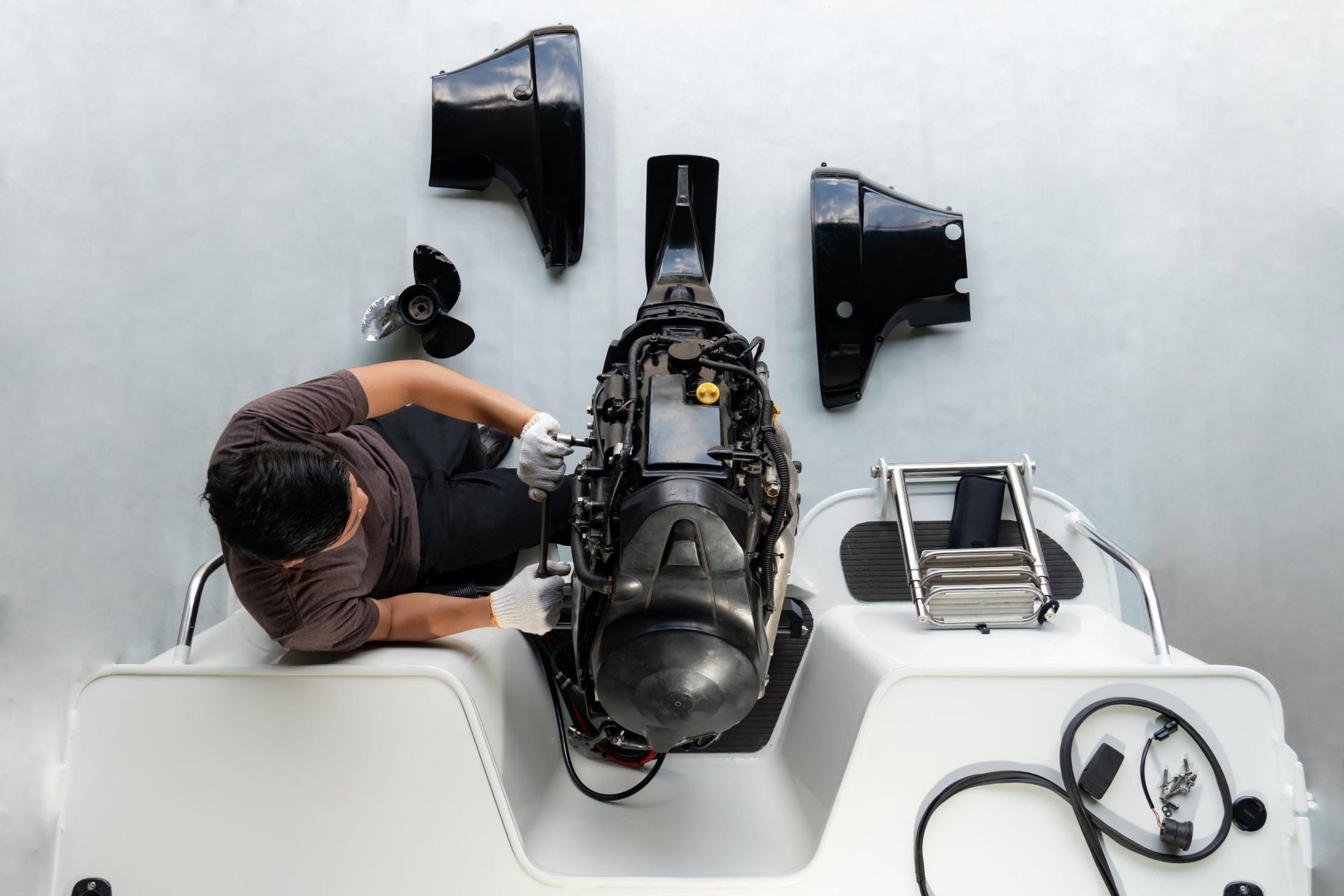 Man working on a boat motor; parts laid out; white boat interior.