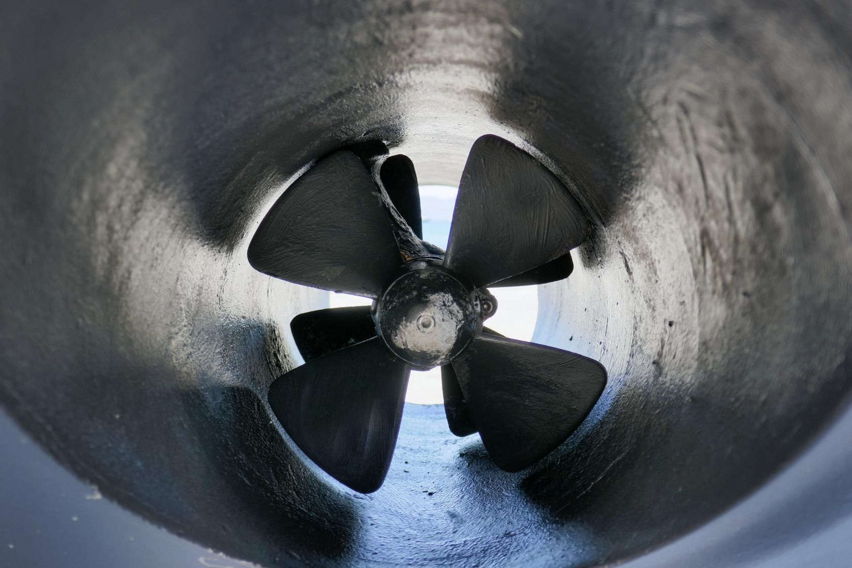 A four-bladed boat propeller inside a dark, cylindrical tunnel.