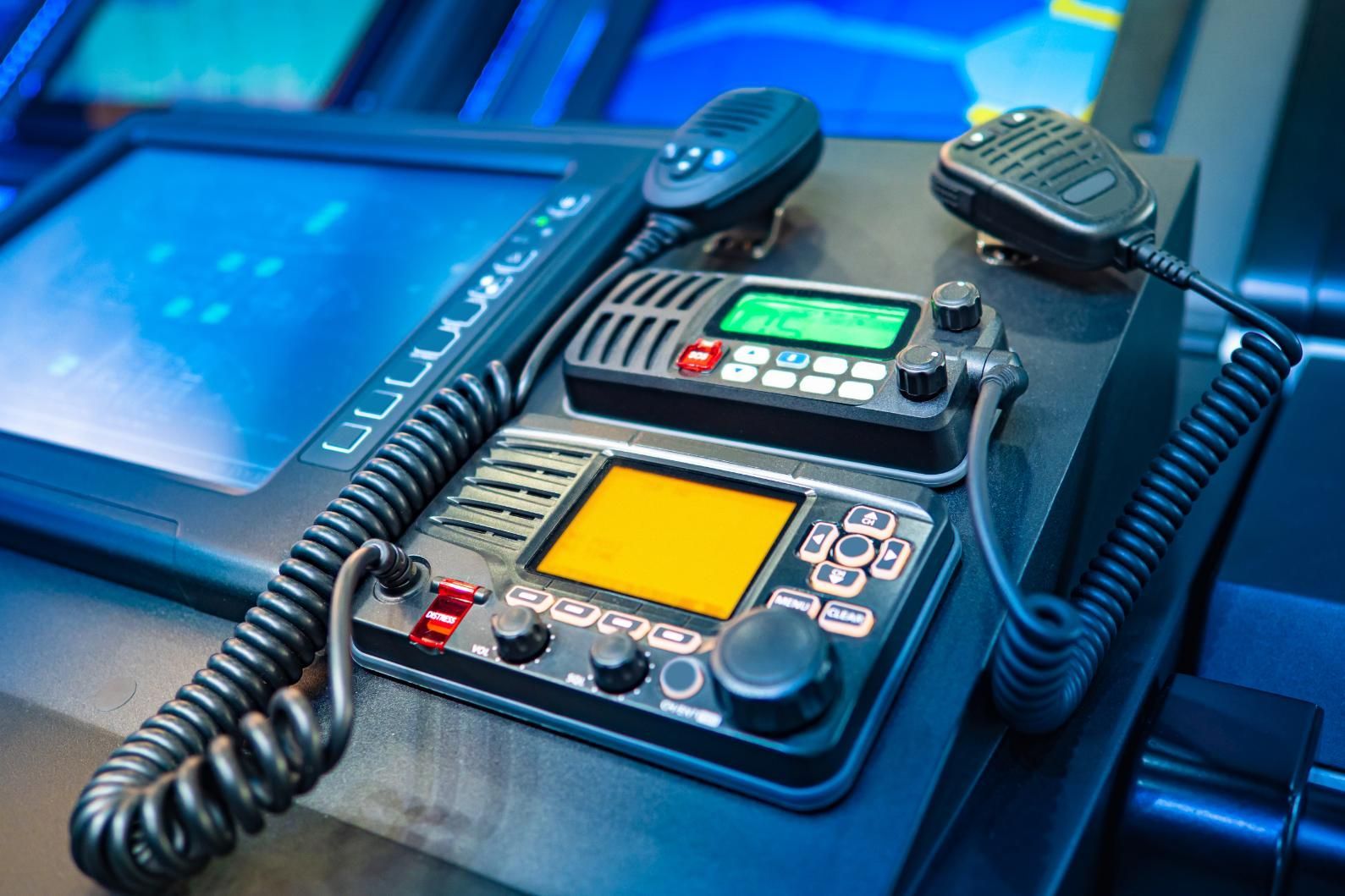 Close-up of a ship's communication equipment, featuring radios with displays, control knobs, and attached microphones.