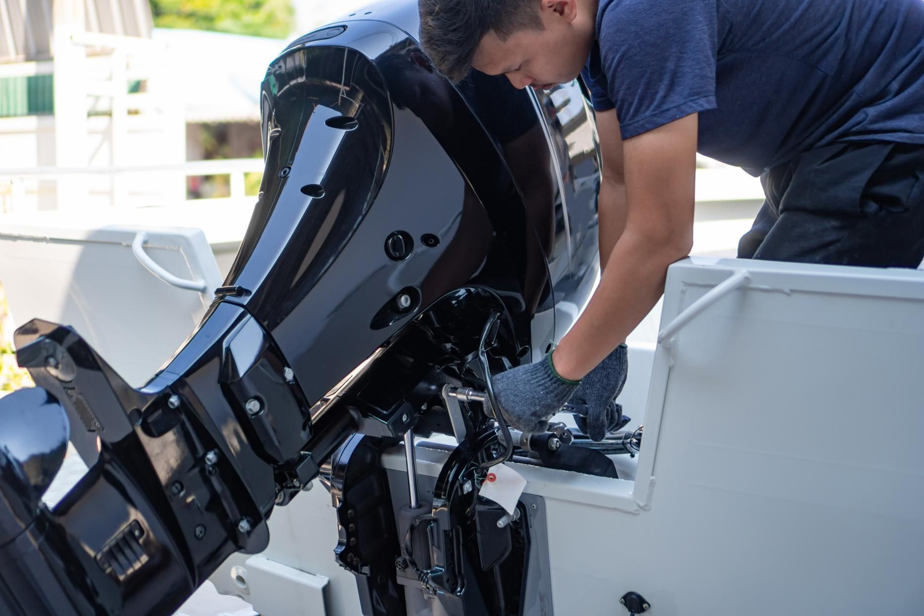 Man working on a black boat motor attached to a light gray boat.