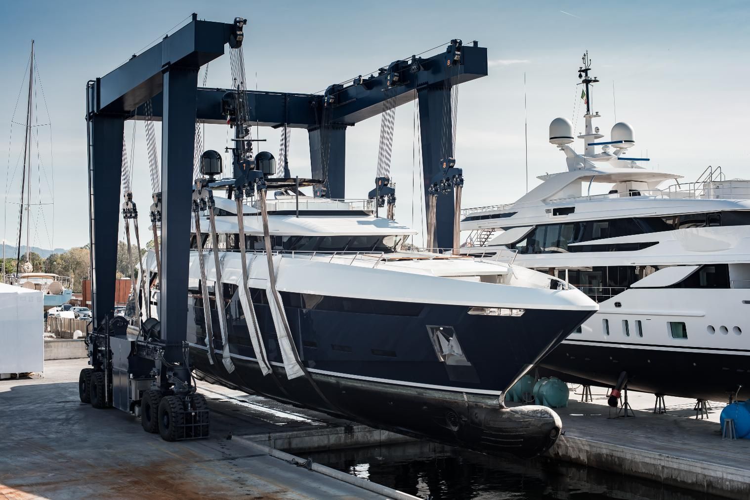 Large yacht being lifted from the water by a mobile boat lift at a marina.