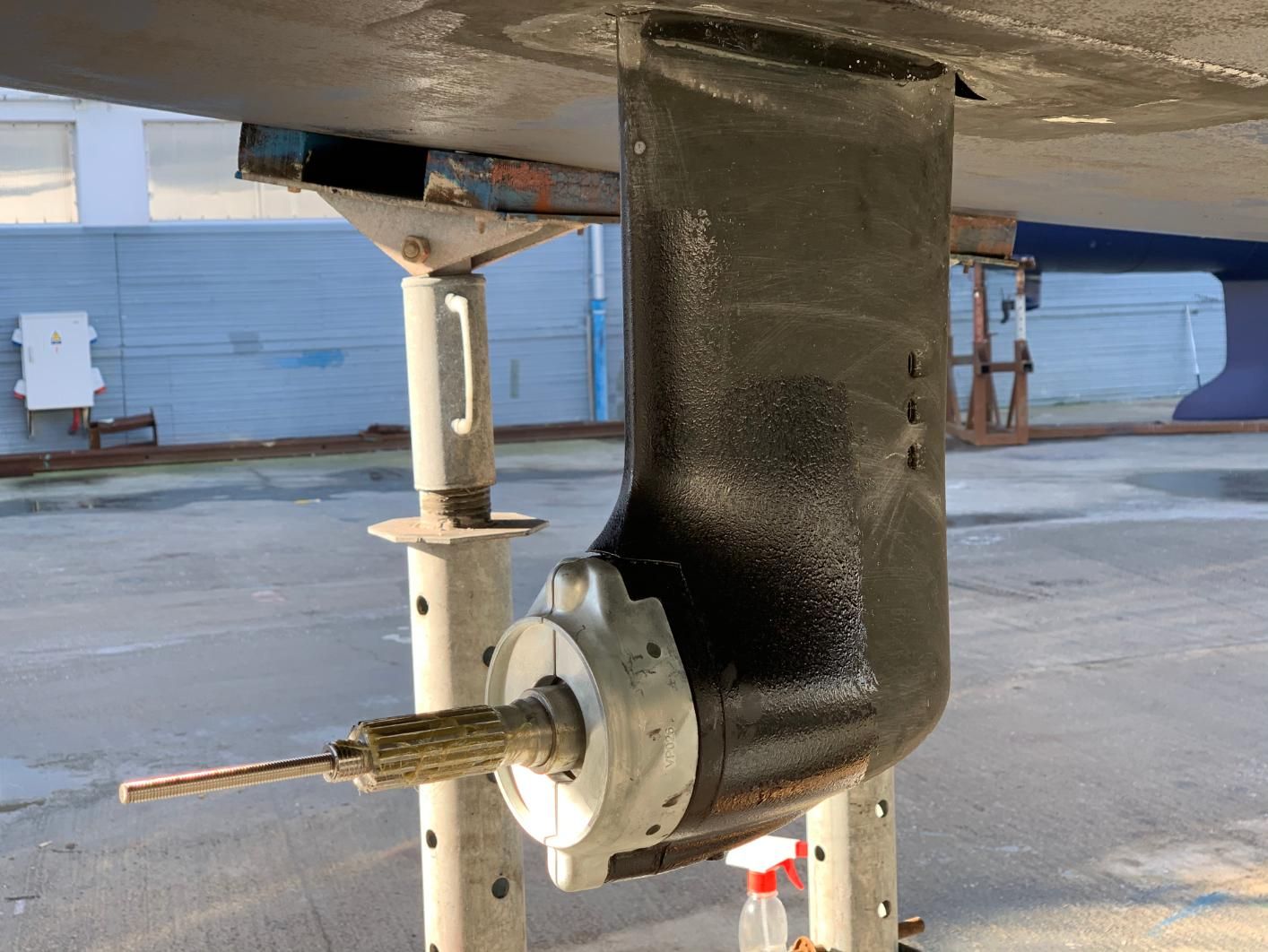 Black boat propeller assembly on a boat hull, supported by metal stands, outdoors.