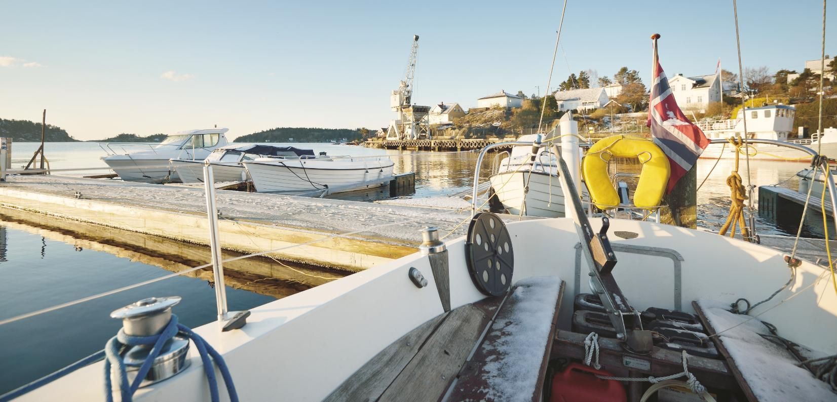 A sailboat on a dock with other boats, a harbor, and buildings in the background.