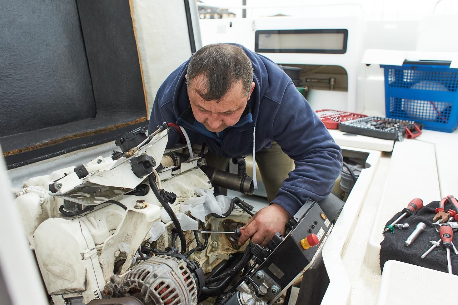 Man working on a boat engine, using a screwdriver, inside the boat.