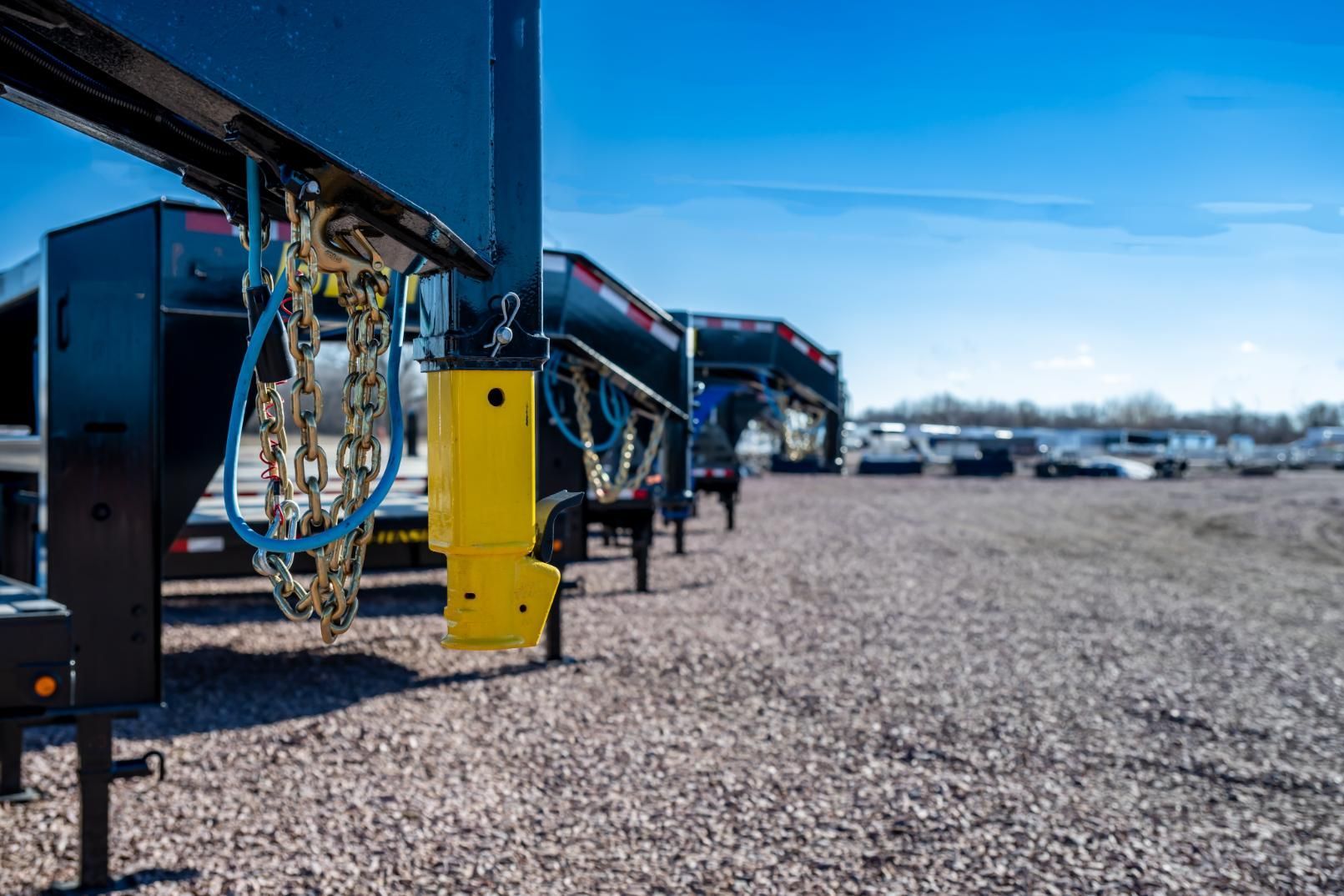 Black trailer with yellow support on gravel, other trailers in the background under a blue sky.