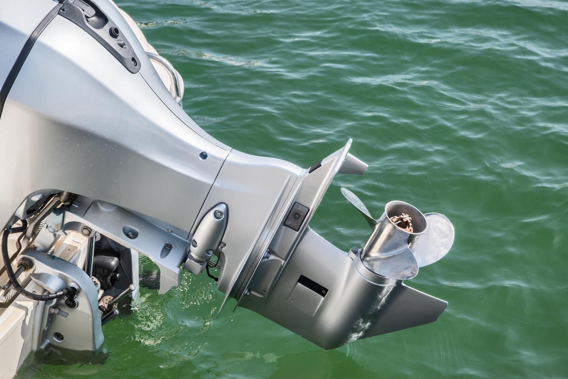 Silver outboard motor in water, propeller turning.