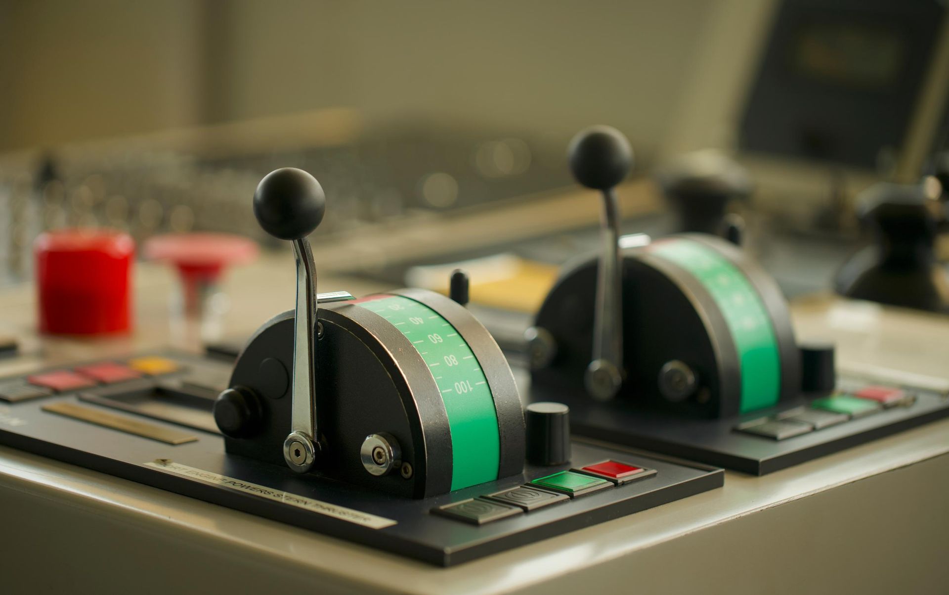 Close-up of ship engine controls with black handles, green indicators, and small buttons on a control panel.
