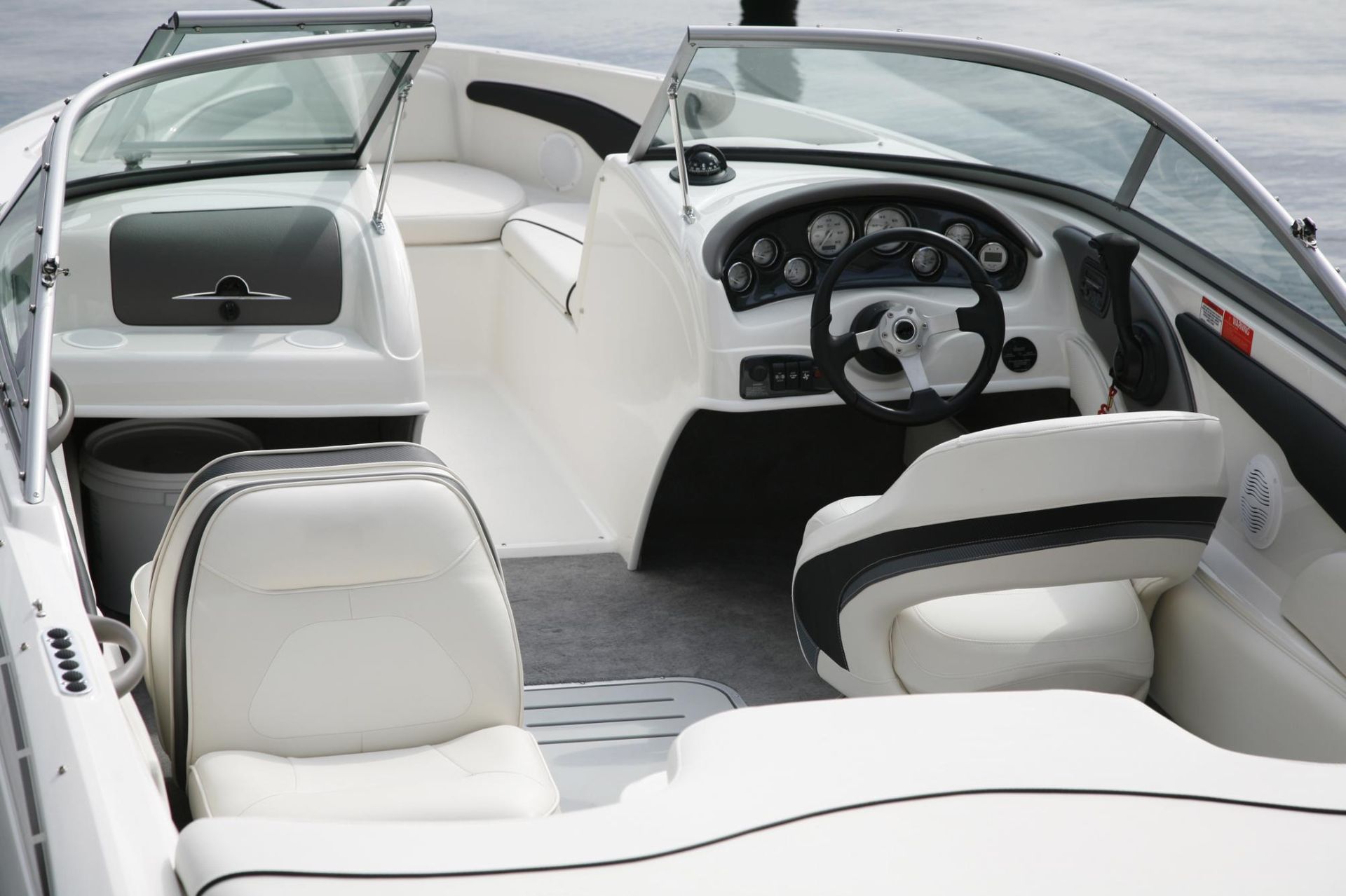 Interior of a white boat with steering wheel, gauges, seats, and windshield.