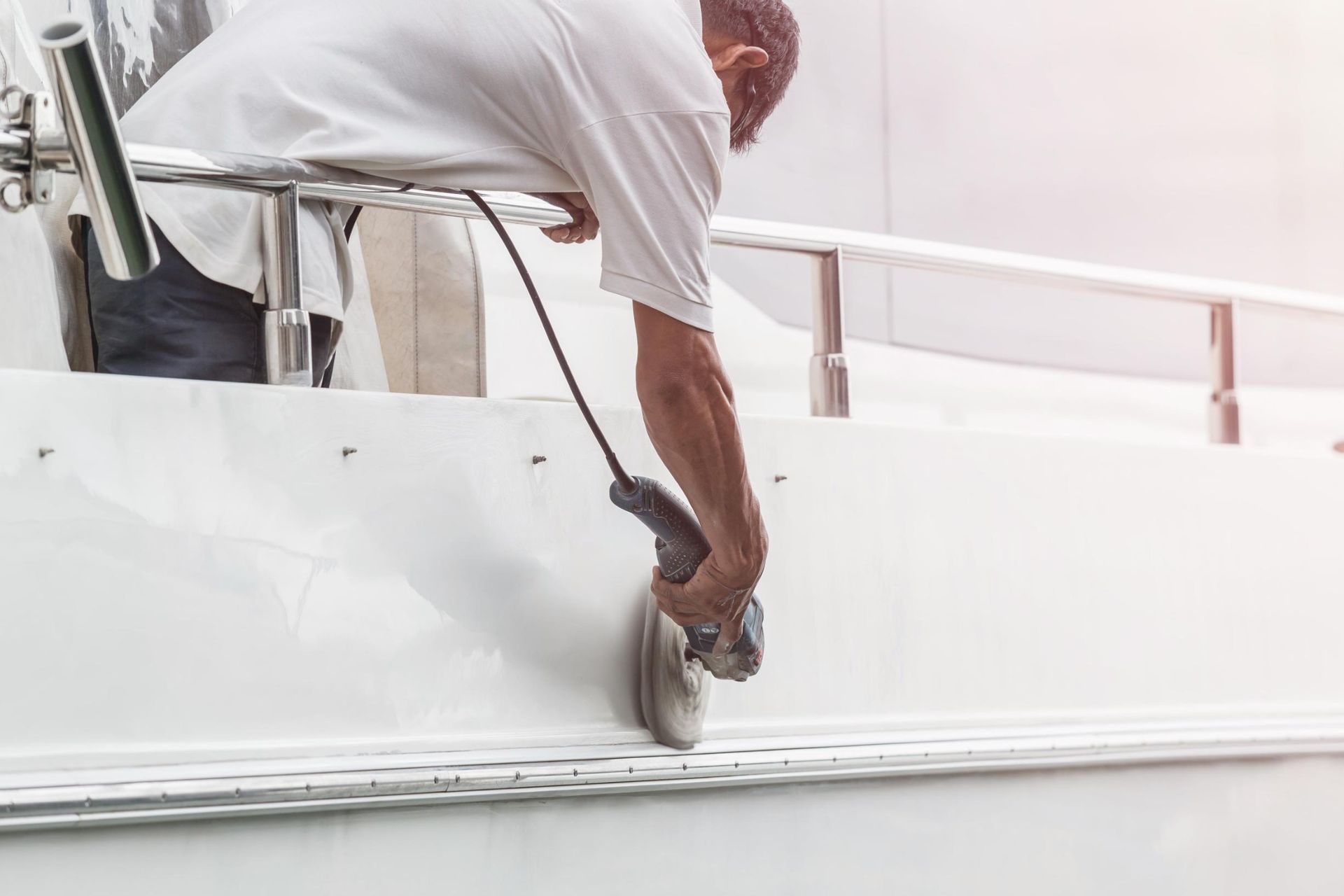Person using a grinder on a white boat near a metal rail.