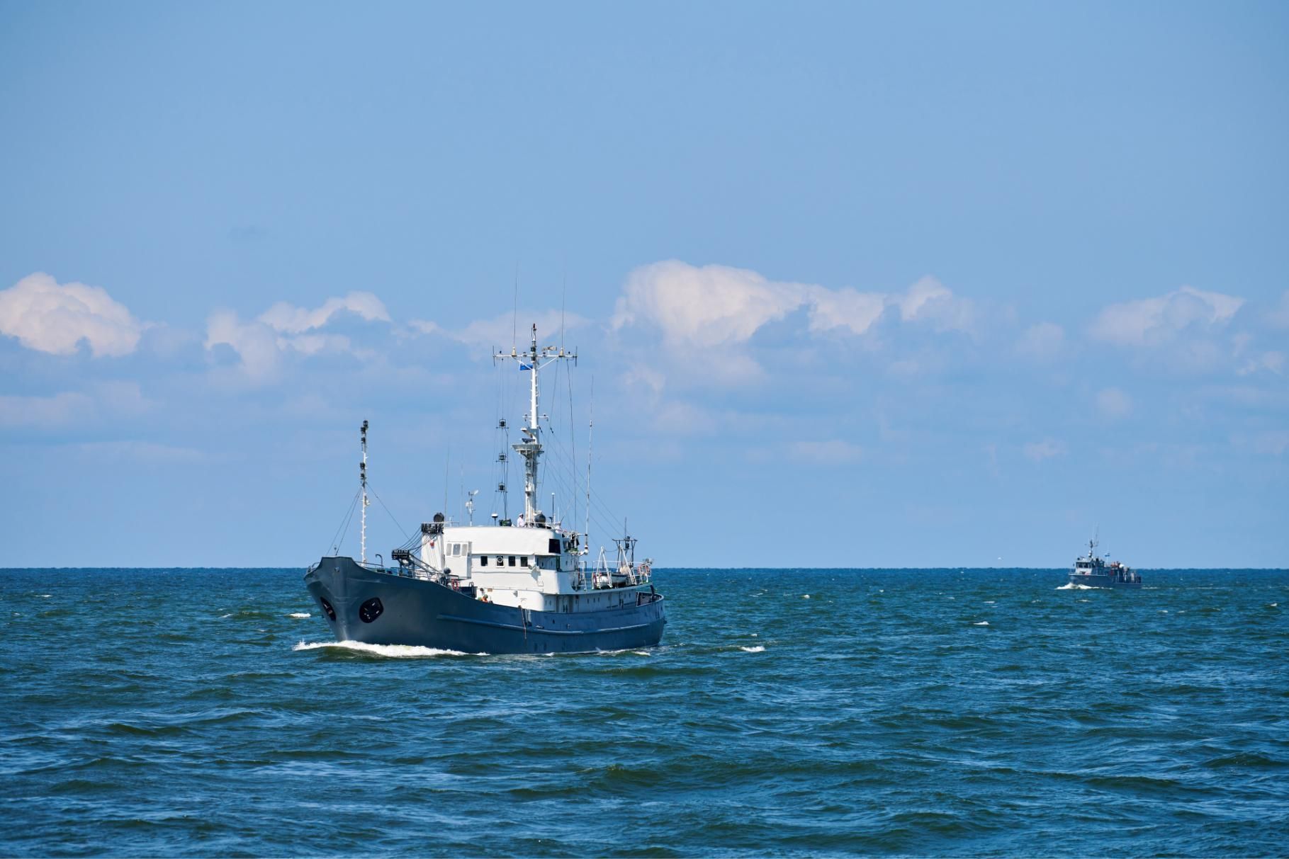 Navy ship sails on blue ocean under a partly cloudy sky.