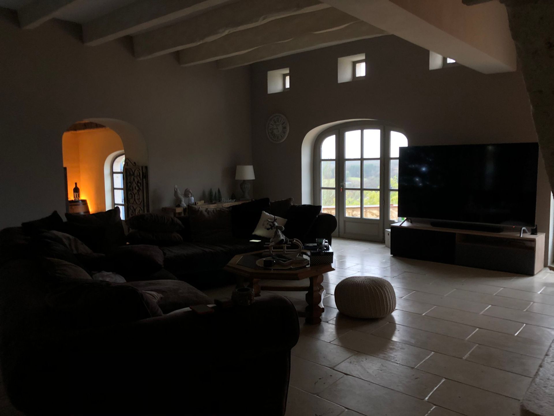 Salon avec un grand canapé foncé, une télévision et des portes cintrées, offrant une vue dégagée sur l'extérieur.