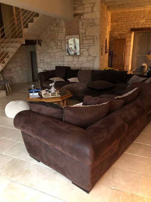 Grand canapé d'angle marron dans un salon avec murs en pierre et escalier.