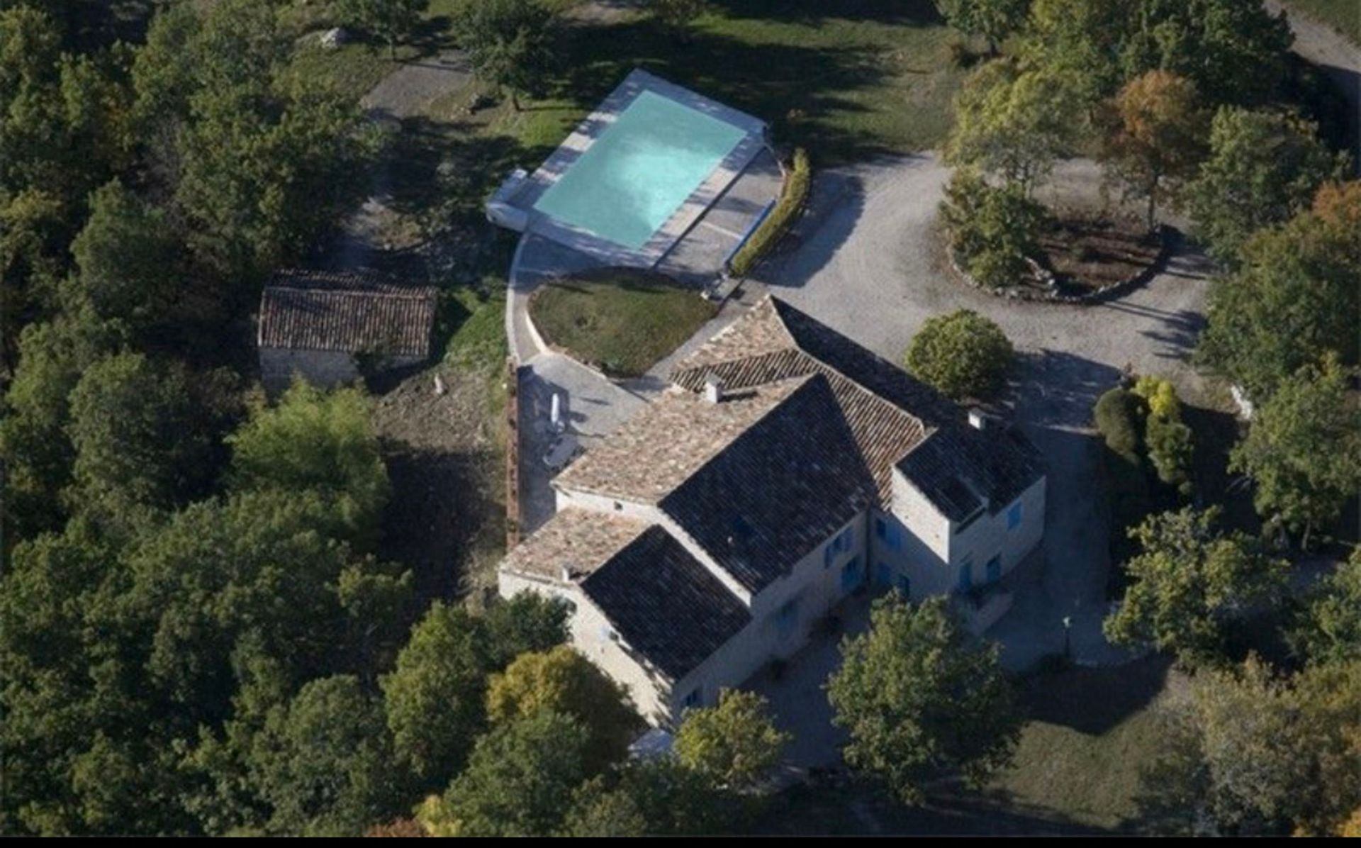 Vue aérienne d'une maison avec piscine entourée d'arbres.