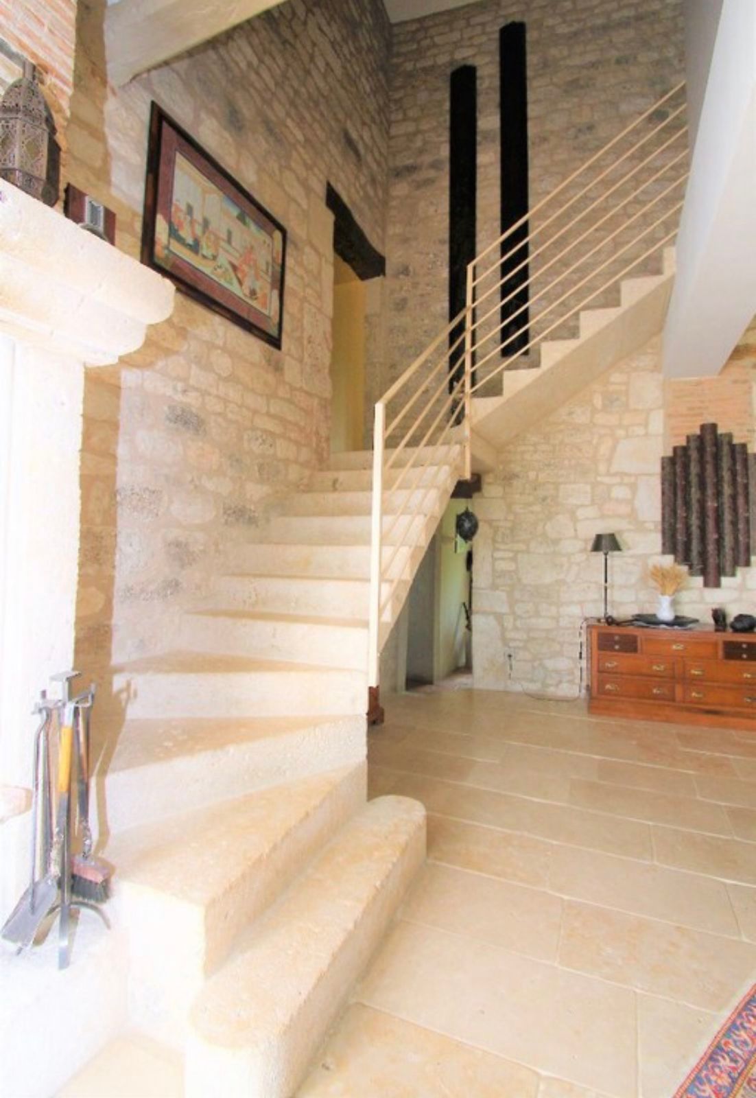 Escalier en pierre avec rampe en métal dans une pièce aux murs en pierre et avec une armoire en bois.