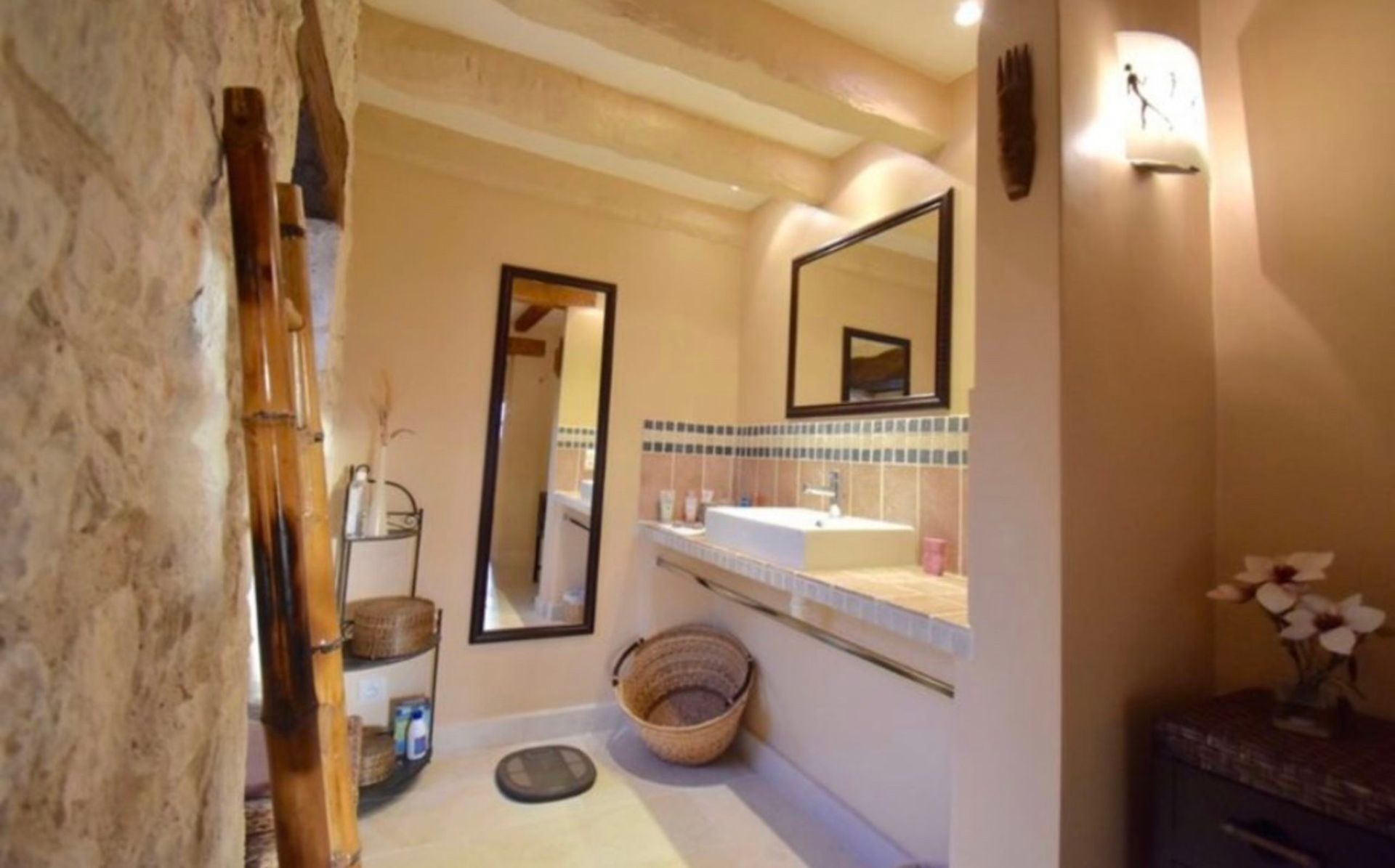 Salle de bains avec murs en pierre, un grand miroir, un lavabo et une échelle rustique appuyée contre un mur.