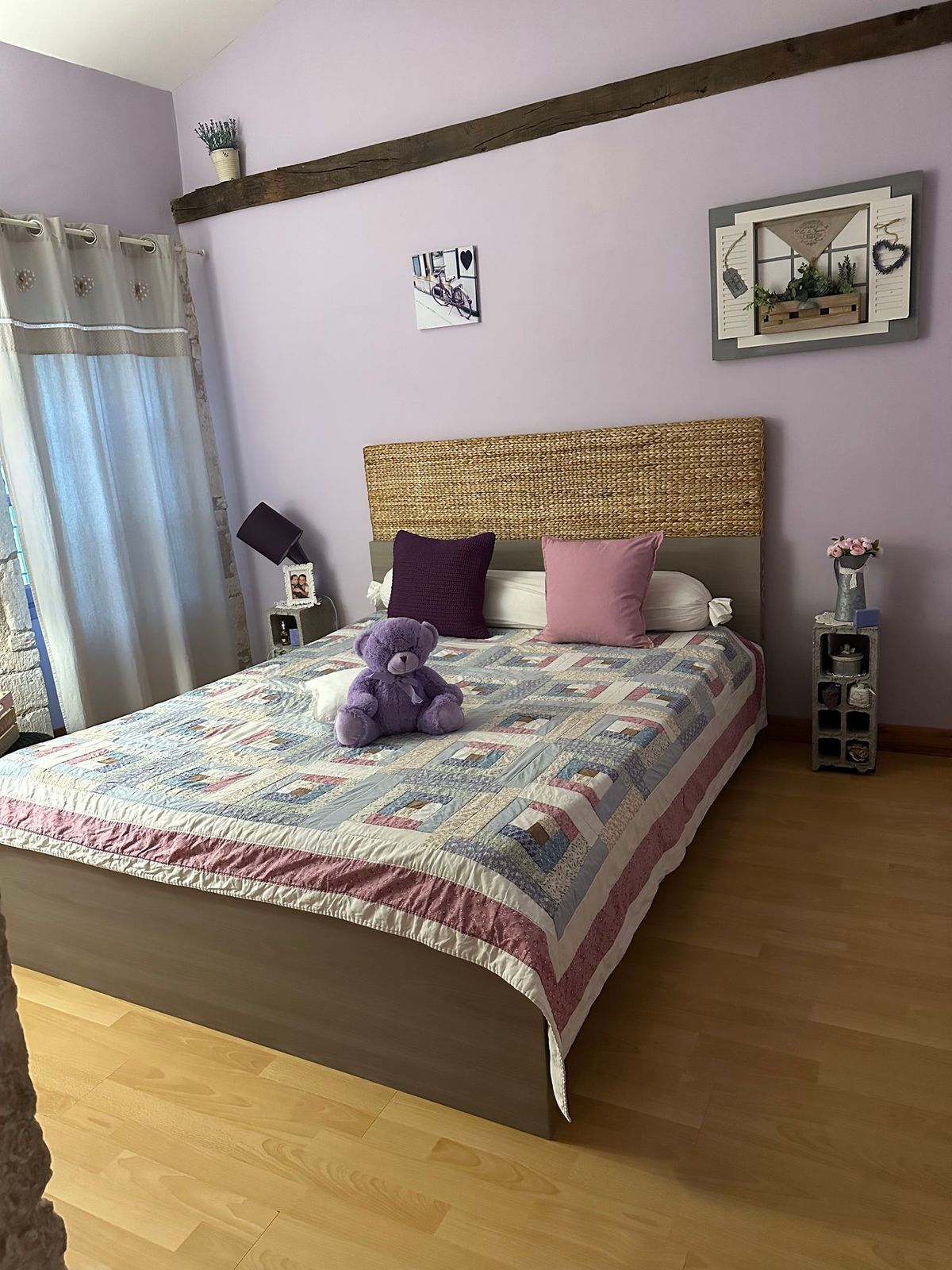 Chambre aux murs lilas, lit recouvert d'une couette à fleurs, ours en peluche et objets décoratifs.