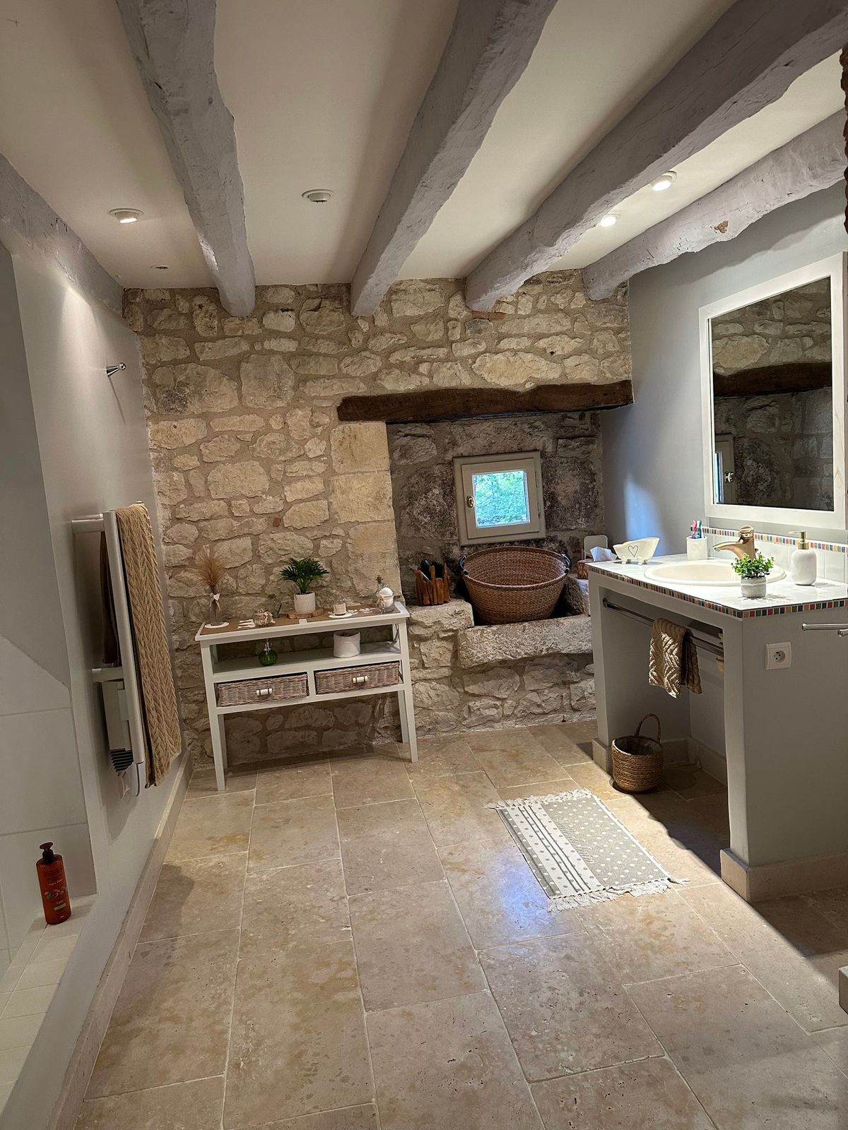 Salle de bains rustique avec murs en pierre, poutres en bois, meuble-lavabo et fenêtre.