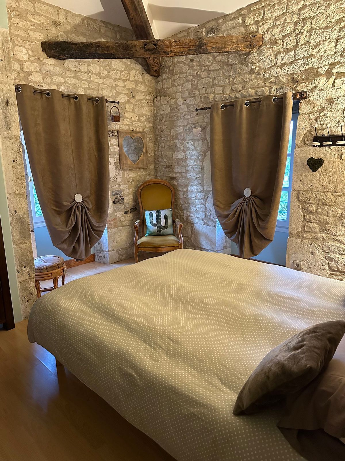 Chambre avec murs en pierre, rideaux marron, lit et chaise jaune.