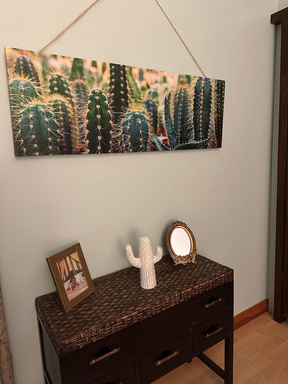 Une œuvre d'art sur le thème du cactus est accrochée au-dessus d'une armoire brun foncé au plateau imprimé léopard, qui contient une figurine de cactus et un miroir.
