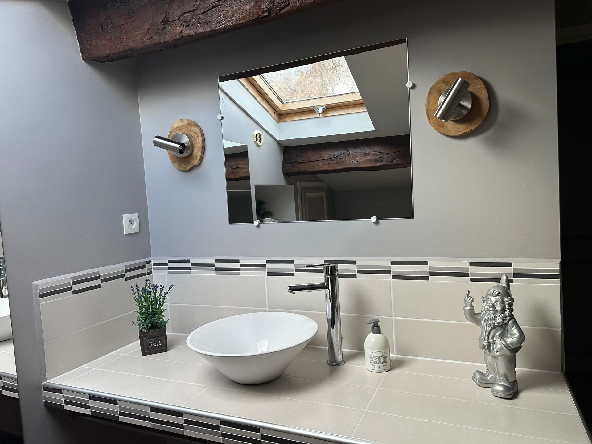 Meuble-lavabo avec vasque ronde, miroir et nain de jardin décoratif. Murs gris.