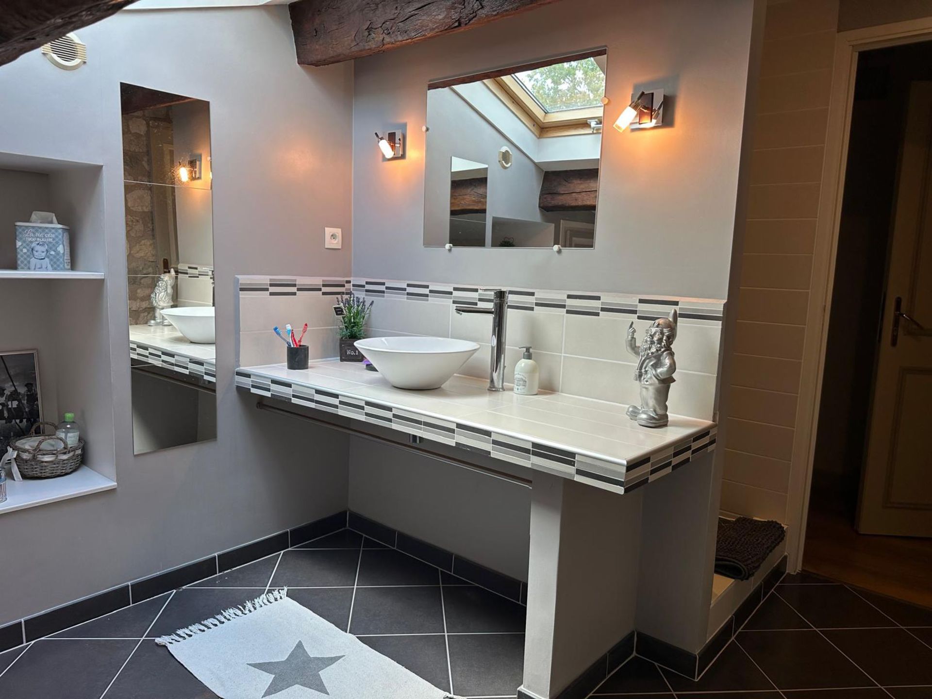 Salle de bains avec lavabo, miroir et sol carrelé, dotée d'un puits de lumière et de murs gris.