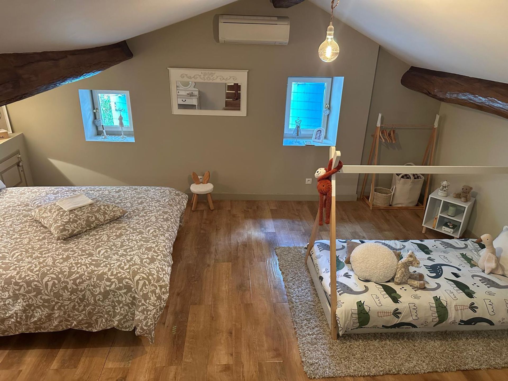 Chambre avec deux lits, parquet, murs gris et poutres apparentes. Un des lits est recouvert d'une couette à motifs.