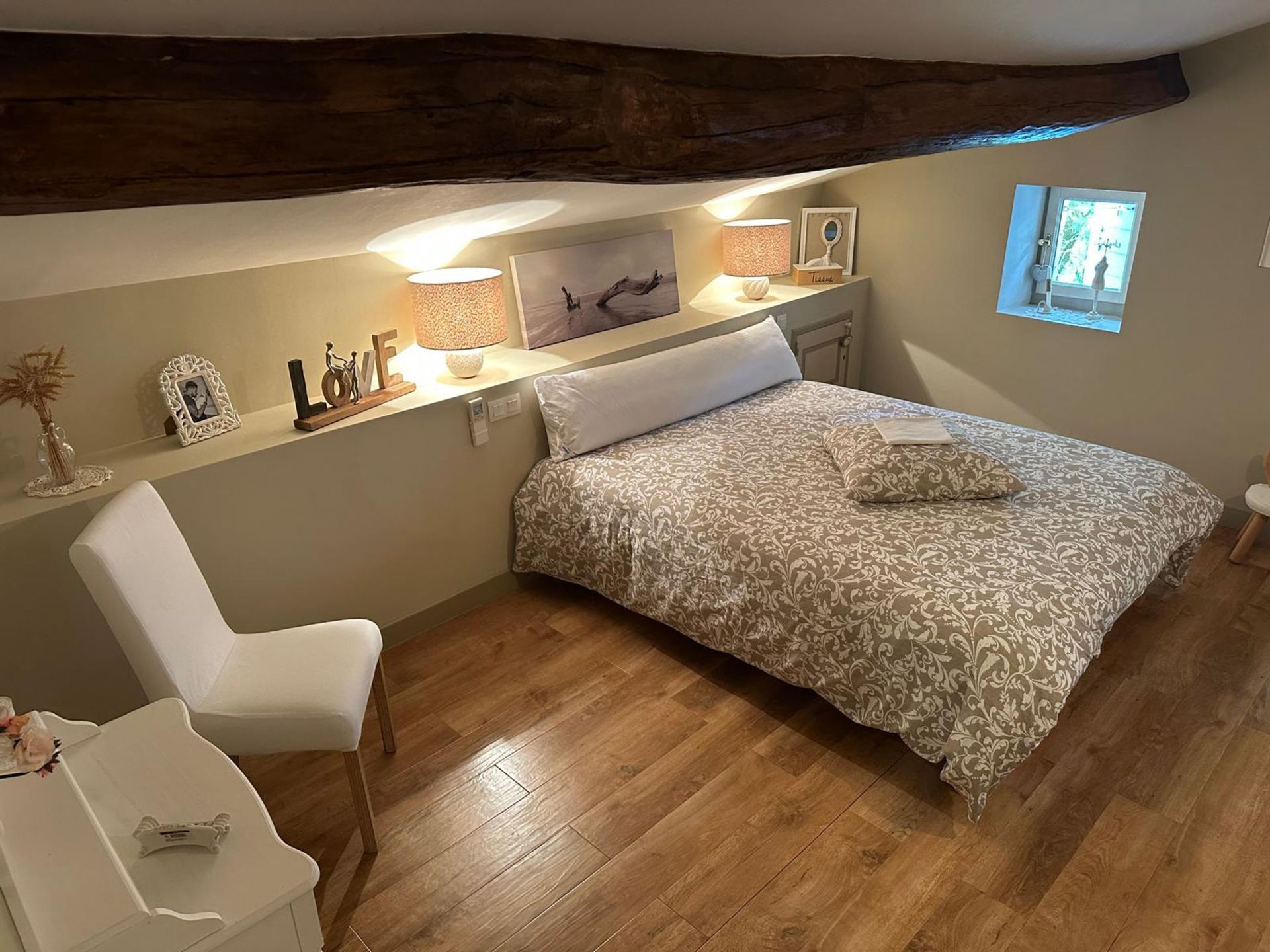 Chambre avec lit, chaise et petite fenêtre. Parquet et éclairage décoratif.
