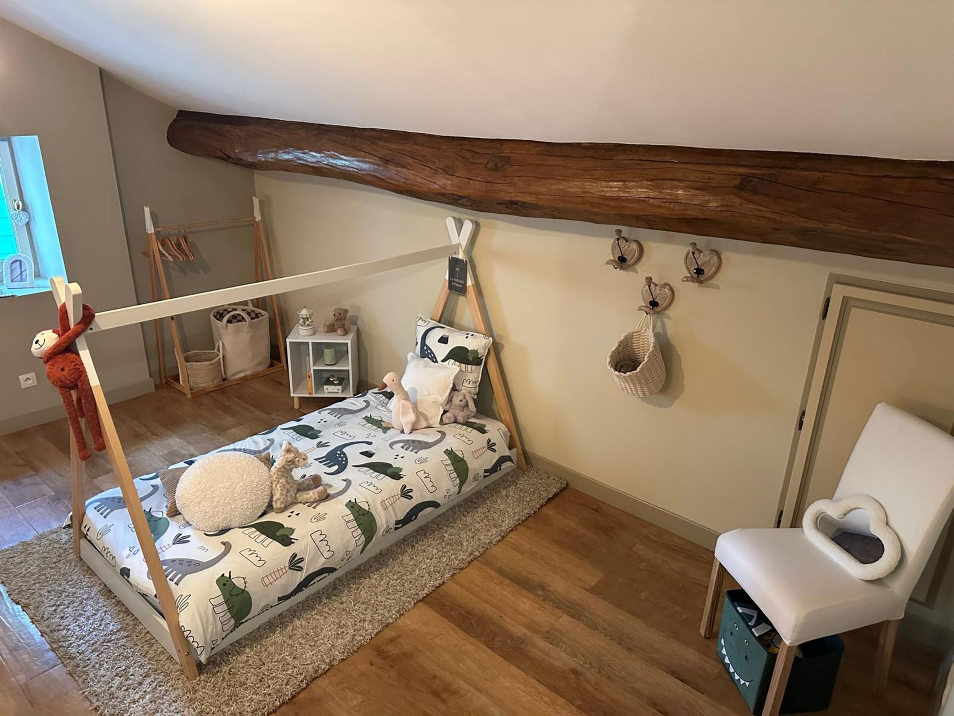 Une chambre d'enfant avec un lit tipi, un tapis et une chaise sur un parquet sous un plafond mansardé.