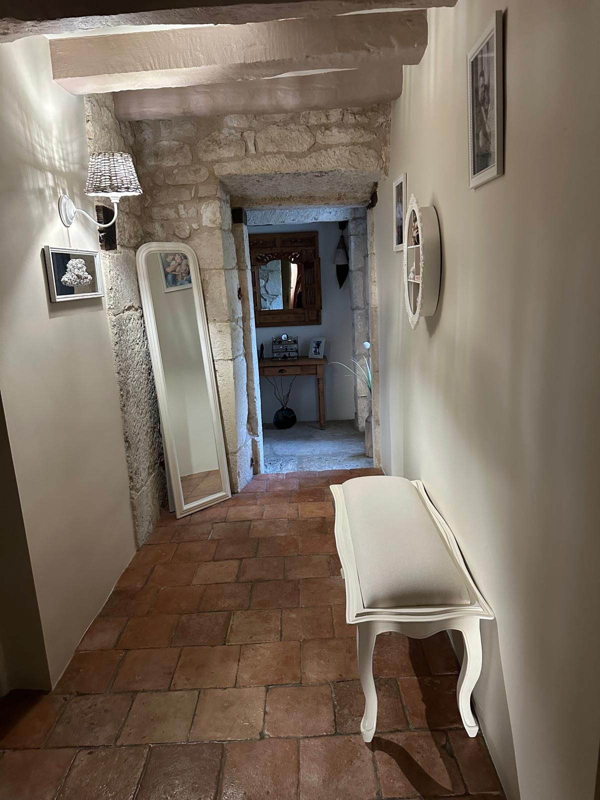 Couloir étroit avec sol en briques, mur en pierre, banc blanc et miroir.