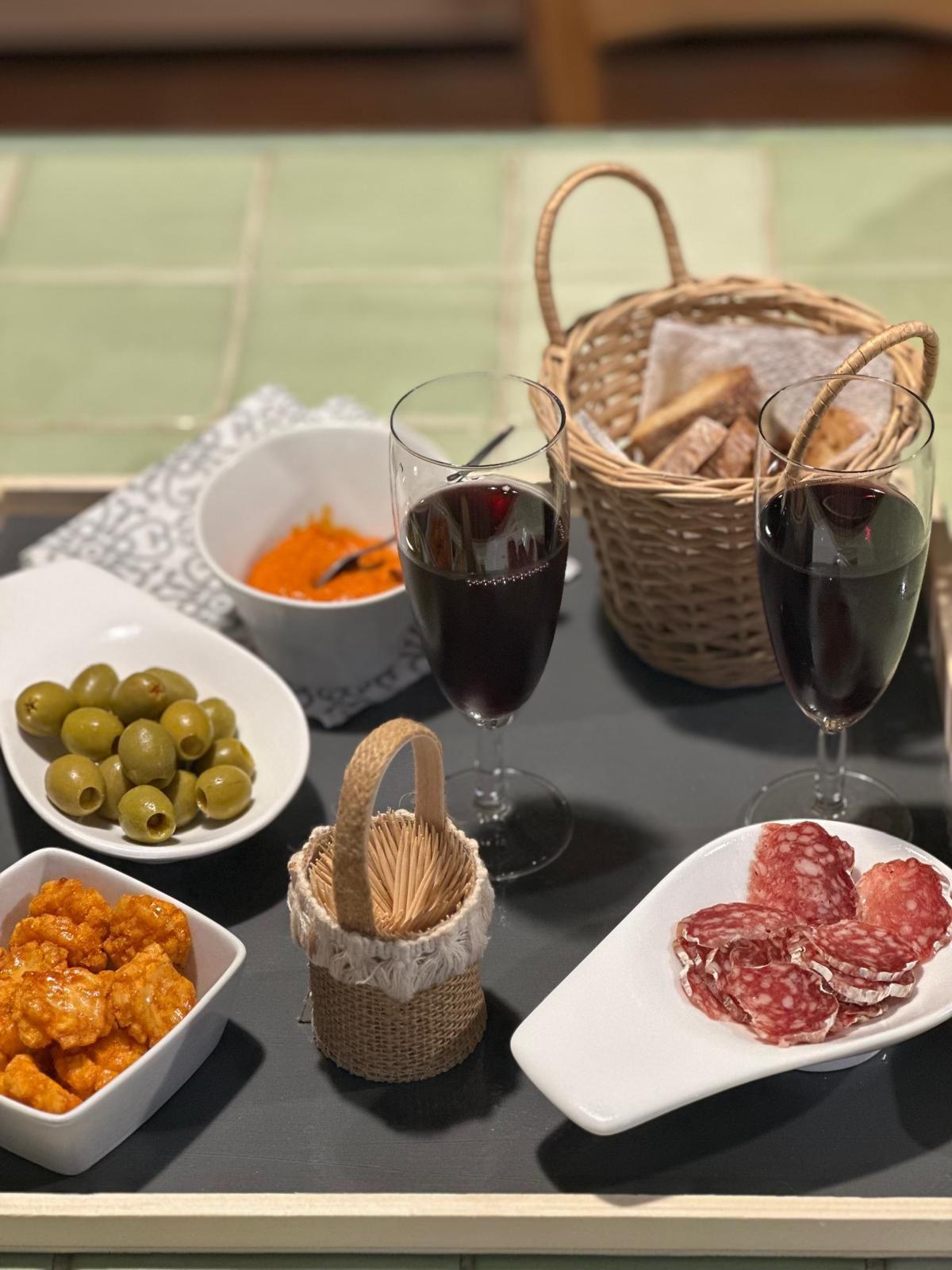 Plateau de charcuterie et de vin : olives, crackers, sauce, pain, salami et deux verres de vin rouge.