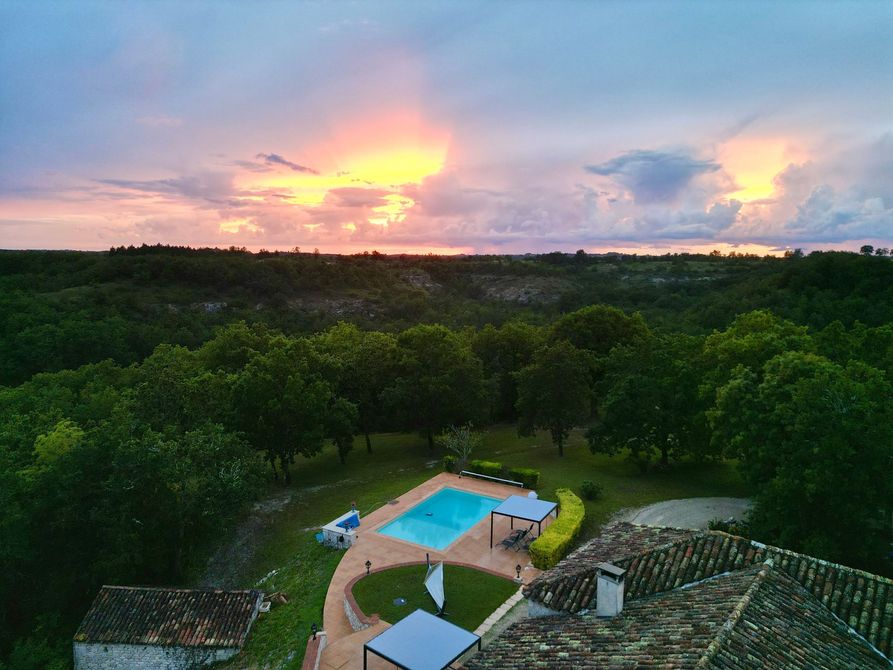 Coucher de soleil sur un paysage verdoyant avec une piscine, des arbres et des bâtiments.
