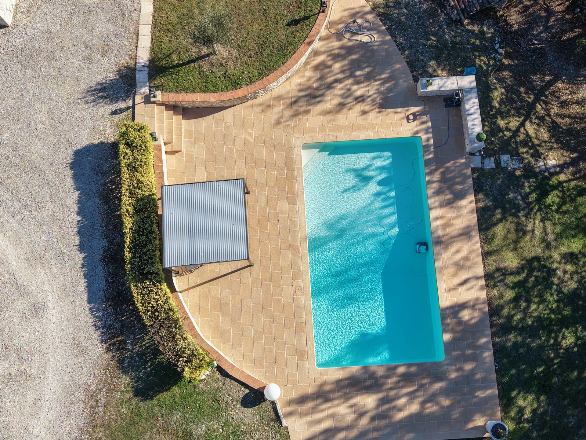 Vue aérienne d'une piscine rectangulaire à l'eau turquoise, d'une terrasse et d'une zone ombragée.