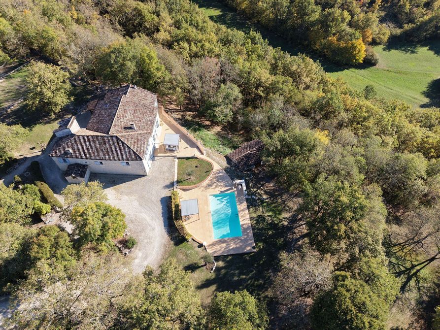 Vue aérienne d'une maison en pierre avec toit en tuiles de terre cuite, piscine et arbres environnants.