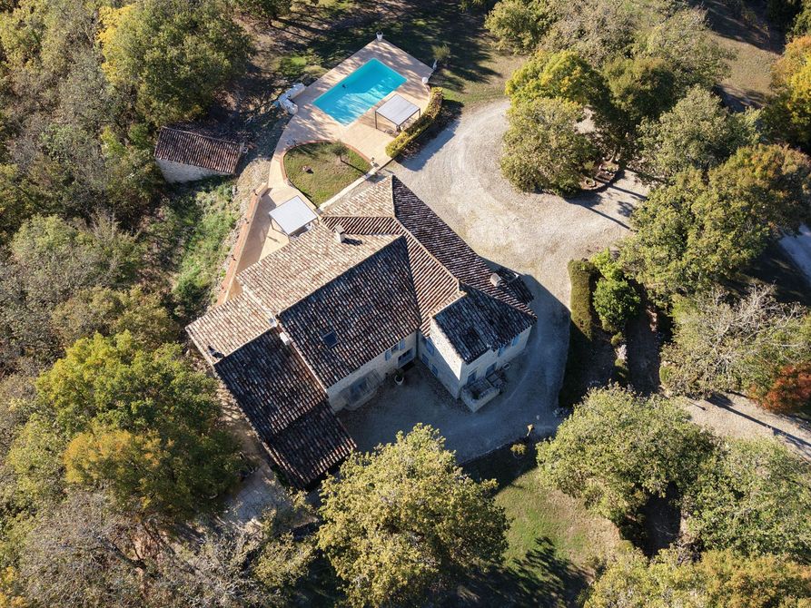 Vue aérienne d'une maison en pierre au toit de tuiles, entourée d'arbres et d'une piscine.