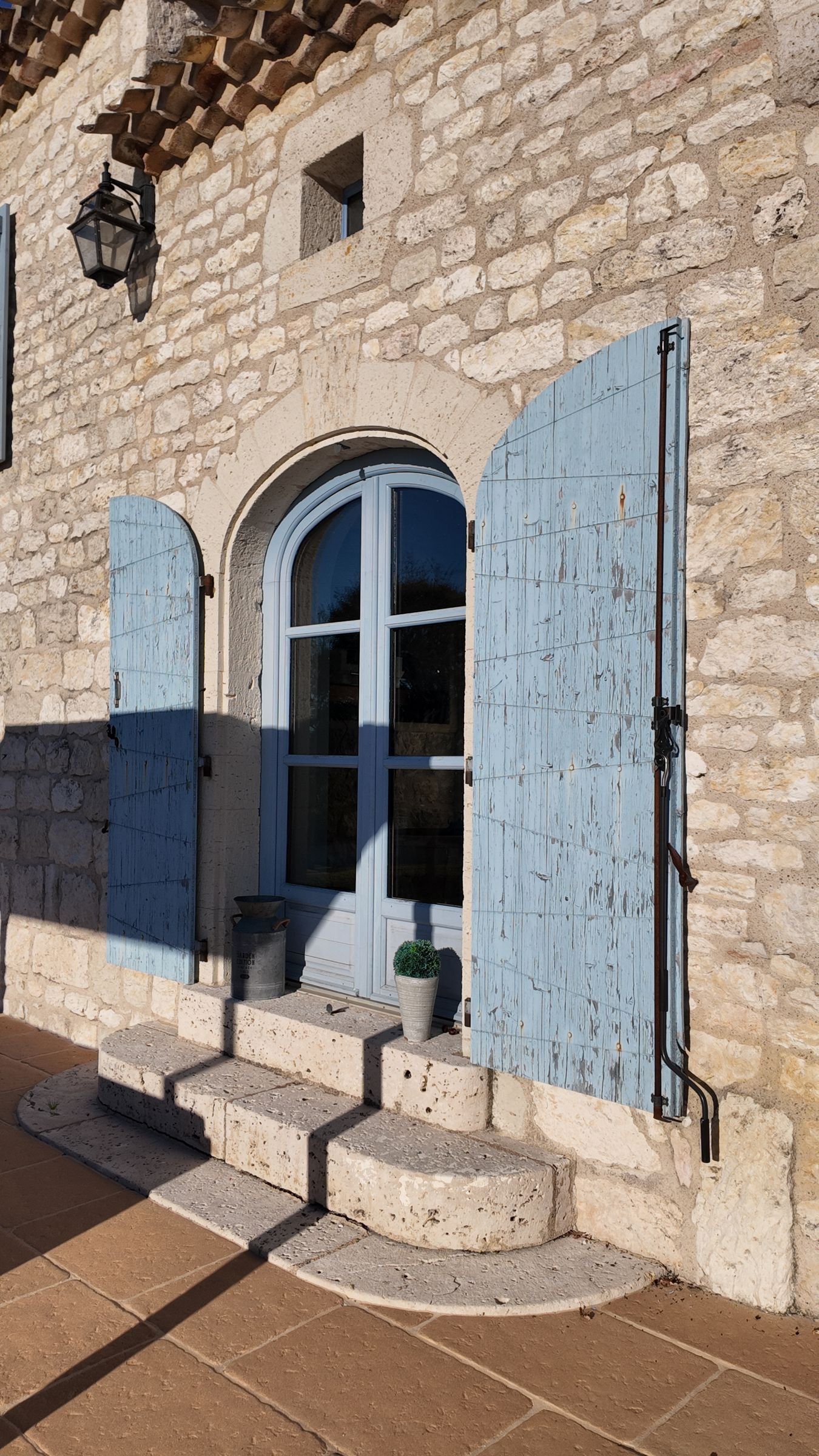 Bâtiment en pierre avec porte et volets bleus ; des marches mènent à l'entrée.