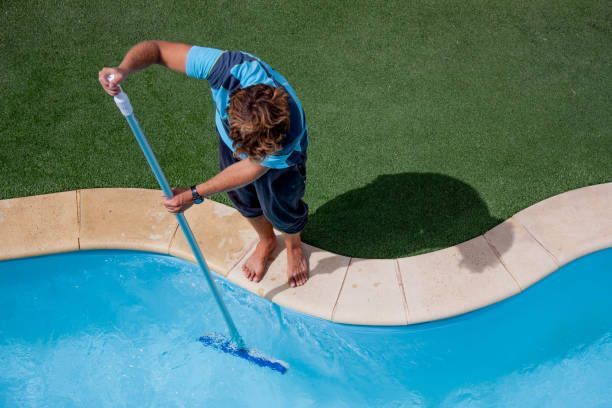 Person cleaning the edge of a swimming pool with a long pole