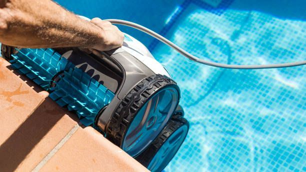 Hand holding a blue pool vacuum cleaning the edge of a swimming pool