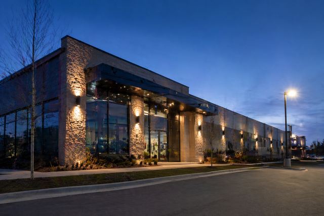 Modern glass-front office building at dusk with warm exterior lights and a streetlamp nearby